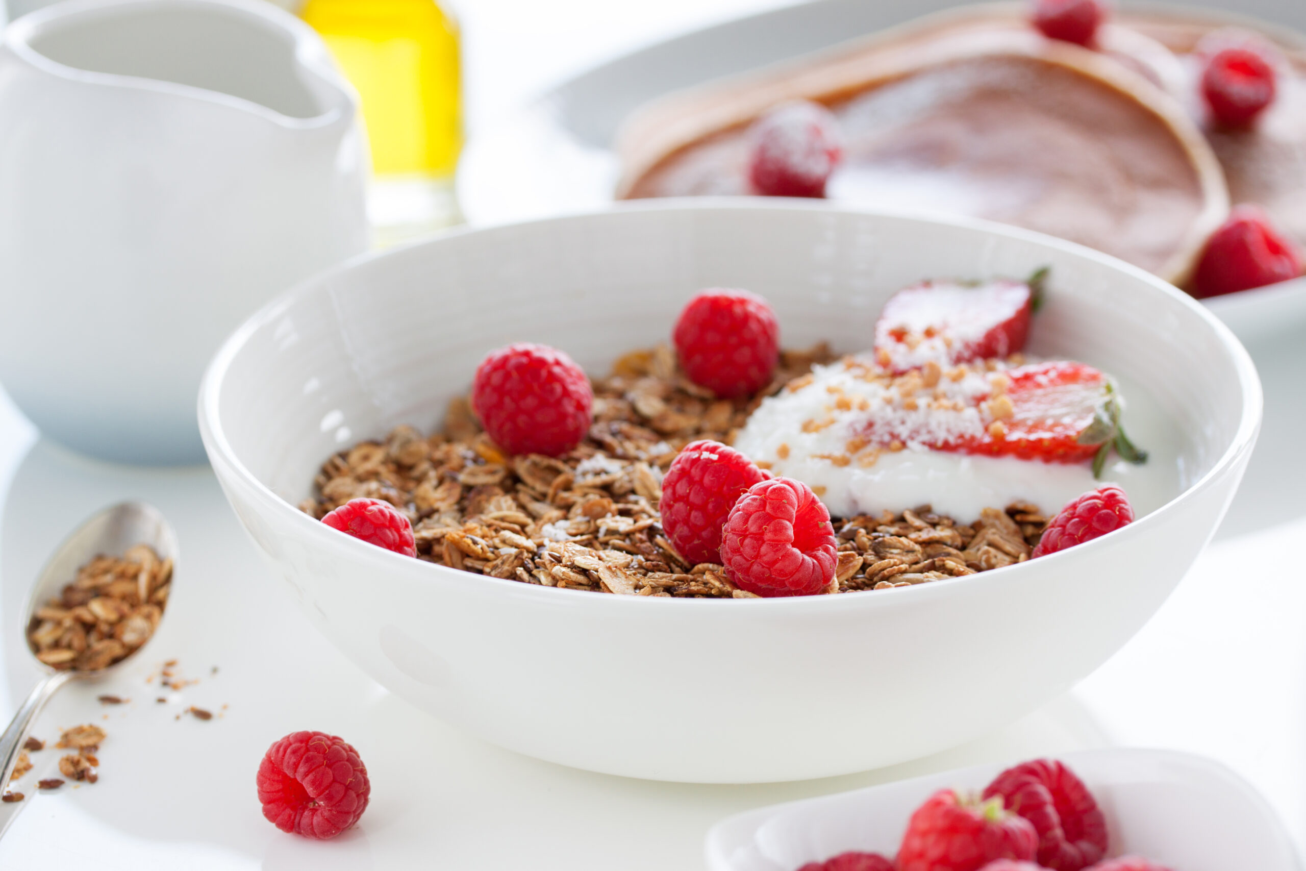 Homemade oat meal granola or muesli with fresh summer fruits – raspberry and strawberry with yogurt in a white bowl on a table for breakfast, closeup